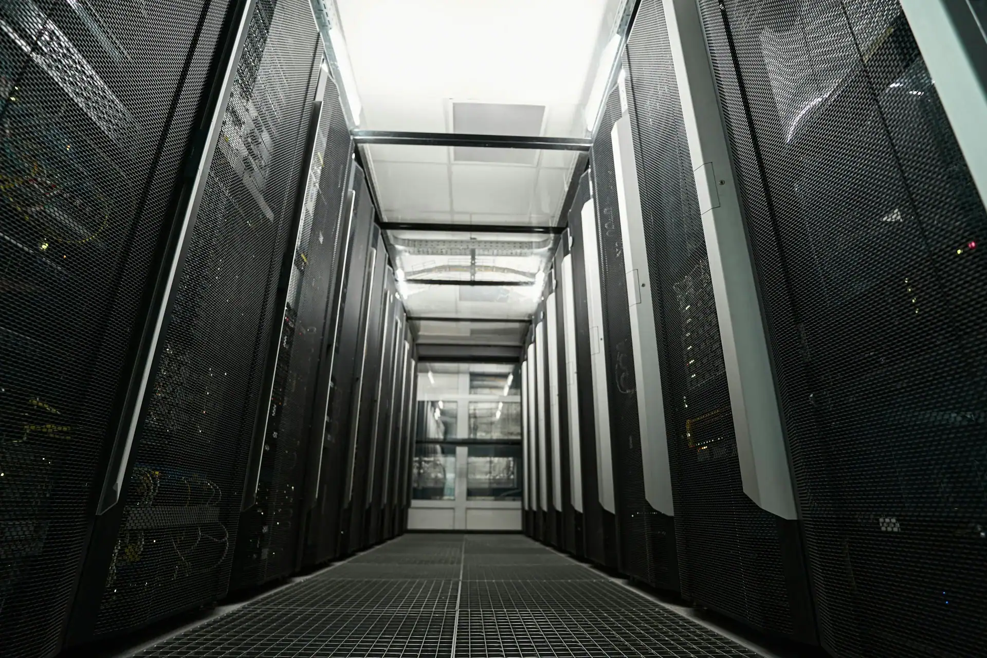 Langer Servergang in einem Rechenzentrum mit zwei Reihen dunkler Server-Racks und Gitterfußboden
